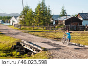 Лето, каникулы, сельская местность, дома, улица, девочка с велосипедом. Поселок Сордоннох , или Орто-Балаган в Якутии ( Республика САХА, Оймяконский район ). Сам Оймяконский район, как и все его села, очень далеко расположены от Большой Земли, и жизнь здесь неторопливая (2010 год). Редакционное фото, фотограф Павел Просянов / Фотобанк Лори