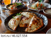 Delicious empanadas served on plate with side salads in background on wooden table. Стоковое AI-изображение, AI-художник Иван Рябоконь / Фотобанк Лори