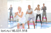 Elderly woman during Pilates strength training performs squats with elastic band on legs and shins. Стоковое видео, видеограф Яков Филимонов / Фотобанк Лори
