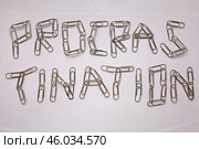 Слово "Прокрастинация", выложенное из металлических канцелярских скрепок на английском языке на белых листах бумаги. Стоковое фото, фотограф Дмитрий Кравченко / Фотобанк Лори