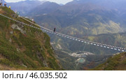 Active recreation in the Caucasus: tourists carefully walk along the suspension bridge at Rosa Peak Mountain. Активный отдых на Кавказе: Туристы осторожно идут по подвесному мосту у горы Роза Пик. Редакционное видео, видеограф Валерий Тесаков / Фотобанк Лори