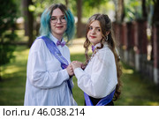 Two joyful graduates with sashes celebrate their graduation day by holding hands in a park. Стоковое фото, фотограф Mikhail Davidovich / Фотобанк Лори
