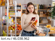 Girl customer holds bottle of peach juice in hand, scans QR code on product label. Стоковое фото, фотограф Яков Филимонов / Фотобанк Лори