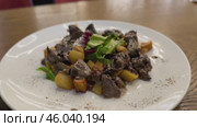 Warm salad with chicken liver in cream sauce with fried potatoes, mushrooms and mixed green salad in a white porcelain plate on a brown wooden table in an elite restaurant. Стоковое видео, видеограф worker / Фотобанк Лори