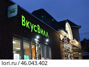 Горящие зелёным светом вывески ВкусВилл и Кофе с собой на одноэтажном здании с хулиганской надписью на крыше вечером, продуктовый магазин с приоткрытой дверью в Красногорске. Редакционное фото, фотограф Алиса Сокол / Фотобанк Лори