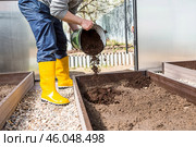 A male farmer pours new soil, soil for a new greenhouse. The concept of spring vegetable planting, greenhouse installation and farming. Стоковое фото, фотограф Photojuli / Фотобанк Лори