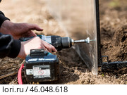 A man holds a battery-powered screwdriver and assembles a new greenhouse made of polyethylene, polycarbonate. Macro photography. Side view. Preparing for the spring garden season. Стоковое фото, фотограф Photojuli / Фотобанк Лори