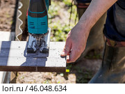 A man holds a battery-powered electric saw and builds new beds in a greenhouse made of wood-polymer composite. Macro photography. Side view. Preparing for the spring garden season. Стоковое фото, фотограф Photojuli / Фотобанк Лори