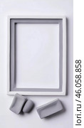 An empty rectangular frame rests against a white gray abstract background. Soft gray clay pieces sit nearby, enhancing the artistic and minimalist aesthetic of the setting. Generative AI. Стоковое AI-изображение, AI-художник Юлия Петровская / Фотобанк Лори