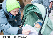 Подросток укрывает младшего брата одеялом в коляске. Старший брат в куртке гуляет с коляской с младенцем в парке весной или зимой. Стоковое фото, фотограф Яна Проничева / Фотобанк Лори