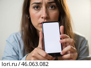 Upset woman holding smartphone mockup with blank screen, close-up of hands and phone, focus on device, casual clothing, technology concept, isolated indoors, front view, selective focus. Стоковое AI-изображение, AI-художник Павел Муравьев / Фотобанк Лори