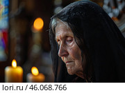 Elderly nun praying in church with veil and candles burning. Стоковое AI-изображение, AI-художник Иван Рябоконь / Фотобанк Лори