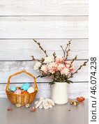 Easter still life with spring bouquet of pussy willow branches and chrysanthemums, traditional painted Easter eggs in a wicker basket and a toy Easter bunny on a gray table. Empty space for text at the top. Стоковое фото, фотограф Виктория Катьянова / Фотобанк Лори