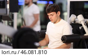 Guy in gym performs exercises for arm muscles using simulators and fitness center equipment. Стоковое видео, видеограф Яков Филимонов / Фотобанк Лори