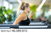A dedicated athlete engages in stretching exercises in a bright and lively gym atmosphere. Стоковое AI-изображение, AI-художник Елена Старчак / Фотобанк Лори