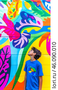 A young boy gazes in awe at a striking mural, surrounded by bright colors and whimsical shapes. Стоковое AI-изображение, AI-художник Елена Старчак / Фотобанк Лори