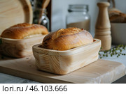 Freshly baked loaf of bread resting in wooden breadbox on kitchen counter. Стоковое AI-изображение, AI-художник Иван Рябоконь / Фотобанк Лори