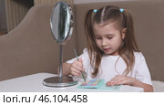 Fashion little girl in a white T-shirt is sitting at the dressing table in front of the mirror and applying makeup with eye shadow. Advertising of children's cosmetics concept. Footage for kids blog. Стоковое видео, видеограф Ирина Михайличенко / Фотобанк Лори