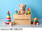 Wooden box with children's toys. A container with a teddy bear and educational wooden toys on a light blue background. Стоковое AI-изображение, AI-художник Photojuli / Фотобанк Лори