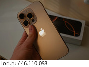 Рука держит смартфон Apple iPhone 16 Pro Пустынный титан на фоне коробка. Редакционное фото, фотограф Башмакова Дарья / Фотобанк Лори