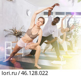 Young woman doing Utthita Parsvakonasana during group yoga workout. Стоковое фото, фотограф Яков Филимонов / Фотобанк Лори