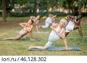 Elderly woman performing Parivrtta Anjaneyasana during group yoga in park. Стоковое фото, фотограф Яков Филимонов / Фотобанк Лори