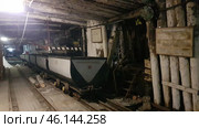 An old mine in Vorkuta, with narrow mine tracks with loaded mine cars on them. You can see the wooden logs that support the tunnel. The walls and ceiling of the mine are dark, covered with soot and traces of dampness, creating the atmosphere of an abandoned or museum object.On the right side there are signs, one of which is called "Mine cars", indicating the museum nature of the exhibition. Above the stairs there is a radiation sign, possibly warning of a possible danger. The stairs lead up into the depths of the tunnel, creating an effect of the unknown.Such mines were key coal mining sites in Vorkuta, playing an important role in the history of the city and the region. This is a reminder of the hard work of the miners, as well as the Gulag era, when prisoners worked in the mines. (2021 год). Редакционное фото, фотограф Анна Кривицкая / Фотобанк Лори