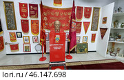 An exhibition of the Soviet era in the USSR Museum, dedicated to the ideology, awards and symbols of the Soviet Union. The central place is occupied by a bust of V.I. Lenin on a red pedestal with the inscription:"V.I. LENIN (ULYANOV) FOUNDED THE USSR IN 1922."Red banners, pennants, awards and portraits of Soviet leaders are placed around. On the walls you can see Soviet slogans, paintings and memorable relics.Red banners with the symbols of the USSR, including the coat of arms and slogans.The bust of Lenin is the central exhibit, surrounded by Soviet paraphernalia.An exhibition of orders and badges, displaying the history of USSR awards.Posters and portraits of leaders (Lenin, Soviet propaganda).Historical relics in glass cases, including dishes, souvenirs and awards.Tapestries and carpets with symbols of the USSR.Retro atmosphere, recreating the spirit of the Soviet era. (2023 год). Редакционное фото, фотограф Анна Кривицкая / Фотобанк Лори