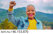 Black mature woman outdoors with raised fist of empowerment, strength and women solidarity, International Womens Day, Black History Month concept. Стоковое AI-изображение, AI-художник Анастасия Золотницкая / Фотобанк Лори
