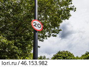 20 mph Speed Limit Road Sign on a Black Pole with Trees and Cloudy Sky in the Background. Стоковое фото, фотограф Zydrius Tartenis / Фотобанк Лори