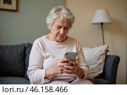 Upset elderly woman sitting on couch, holding phone, visibly distressed after being scammed, emotional reaction to fraud, worried and sad indoors. Стоковое AI-изображение, AI-художник Павел Муравьев / Фотобанк Лори