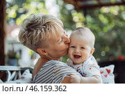 Бабушка обнимает и целует ребенка в щеку, любовь и связь поколений. Стоковое AI-изображение, AI-художник Anna Leeva / Фотобанк Лори