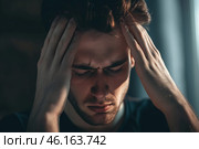 Stressed young man struggling to cope with overwhelming emotions in a dimly lit room during evening hours. Стоковое AI-изображение, AI-художник Sergey Grishin / Фотобанк Лори