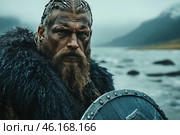 A stern Viking warrior standing against a cold northern landscape. His face is covered in dirt and battle scars, his gaze is full of determination. He is dressed in a heavy fur cape to protect him from the icy wind, and he holds a wooden shield with metal elements. In the background, mountains covered in fog and the northern sea with stones are visible, creating an atmosphere of cruel nature and harsh living conditions of the Vikings. Стоковое AI-изображение, AI-художник Анна Кривицкая / Фотобанк Лори