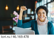Mature middle eastern woman in office with raised fist of empowerment, strength and women solidarity, International Womens Day concept. Стоковое AI-изображение, AI-художник Анастасия Золотницкая / Фотобанк Лори