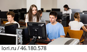 Positive teen girl student talking to concentrated teenager boy studying in computer room. Стоковое фото, фотограф Яков Филимонов / Фотобанк Лори