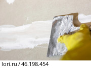 Preparing drywall for plastering. The craftsman cleans and sands the putty from the joints and screws with a spatula. Стоковое фото, фотограф Коханова Наталья / Фотобанк Лори
