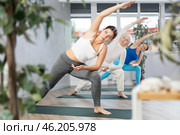 Women of different ages stretching in Extended Side Angle Pose or Utthita Parsvakonasana during yoga class in gym studio. Стоковое фото, фотограф Яков Филимонов / Фотобанк Лори