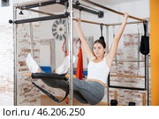 Girl visitor performs exercises in hanging position on combined Pilates trapeze table. Стоковое фото, фотограф Яков Филимонов / Фотобанк Лори