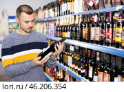Male shopper carefully selects a bottle of wine in wine store. Стоковое фото, фотограф Яков Филимонов / Фотобанк Лори