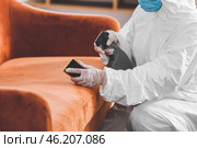 Worker in biohazard costume removing dirt from sofa in house. Стоковое фото, фотограф Pixel_shot / Фотобанк Лори