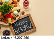 Chalkboard with text HAPPY NOWRUZ, treats, glass of tea and grass on beige background. Стоковое фото, фотограф Pixel_shot / Фотобанк Лори