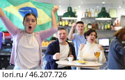 Company of enthusiastic young adult sports fans waving flag of Brazil and supporting national team with beer in pub. Стоковое видео, видеограф Яков Филимонов / Фотобанк Лори