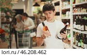 Guy chooses semi-sweet wine while standing near the shelves with alcohol in a hypermarket. European chooses bottles of wine in a store against the background of customers. Стоковое видео, видеограф Яков Филимонов / Фотобанк Лори