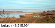 Autumn morning on the Kama River. A dirt road runs along the shoreline. There are thickets of reeds in the water. In the distance behind a small island with trees disperse remnants of fog. Стоковое фото, фотограф Роман Дзюбало / Фотобанк Лори