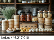 Traditional Chinese cuisine with a variety of dishes and ingredients neatly arranged on the table. The focus is on several types of dim sum, including baozi and xiomai, arranged on a wooden board. Also visible in the foreground are bamboo steamer baskets, typical for steaming.On the right are glass jars with copper lids filled with various dried ingredients, such as nuts or mushrooms. In the center are two jars with pickled or fried snacks. Behind are wooden shelves with dishes, creating the atmosphere of a traditional Chinese kitchen or restaurant.Calm, warm colors and soft lighting make this scene cozy and appetizing. There is also a decorative element - a bouquet of gypsophila, which adds tenderness to the composition. Стоковое AI-изображение, AI-художник Анна Кривицкая / Фотобанк Лори