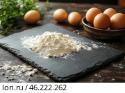 Ingredients for baking: a pile of flour scattered on a black stone board, and several chicken eggs placed around, including in a clay bowl. The background is slightly blurred, with natural wooden elements, creating an atmosphere of coziness and home cooking. The light falls softly, emphasizing the texture of the flour and eggshells. The whole image conveys warmth, simplicity and naturalness, reminiscent of the moments of preparing dough for bread, pies or other culinary products. Стоковое AI-изображение, AI-художник Анна Кривицкая / Фотобанк Лори