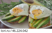 Two Toasts with avocado and fried egg Spreading Yolk, rosemary 4K. Preparing healthy toast breakfast avocado slices rye wholegrain bread, sunny side up egg on top. Healthy breakfast for two, couple. Стоковое видео, видеограф Елизавета Малкова / Фотобанк Лори