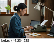 Молодая женщина печатает на ретро-машинке в уютном рабочем уголке с естественным освещением. Рядом находится открытый ноутбук. Стоковое AI-изображение, AI-художник Сергей Никифоров-Гордеев / Фотобанк Лори