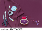 Flat lay of sewing accessories and materials for sew and cutting on burgundy silk fabric - threads, meter, needles, buttons, scissors, pattern, pincushion. Sewing as a hobby. Copy space, top view, close-up. Стоковое фото, фотограф Виктория Катьянова / Фотобанк Лори